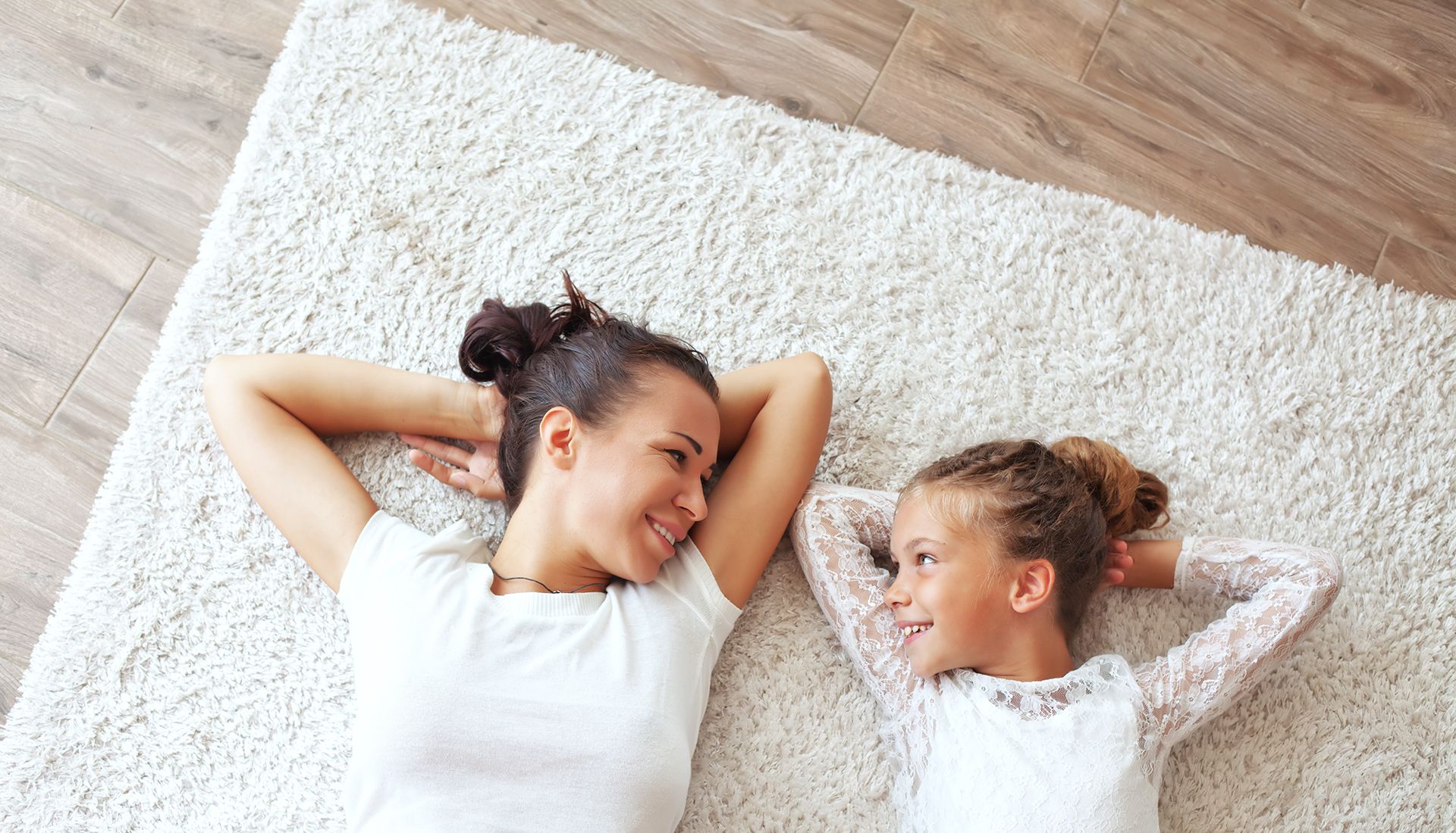 Mother and daughter lying on white rug over hardwood floors